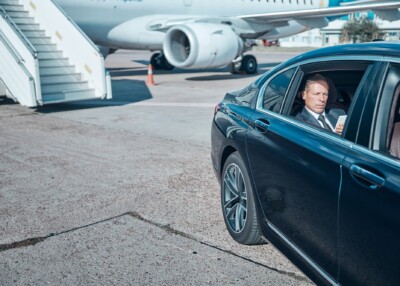 Businessman with smartphone in car at airport